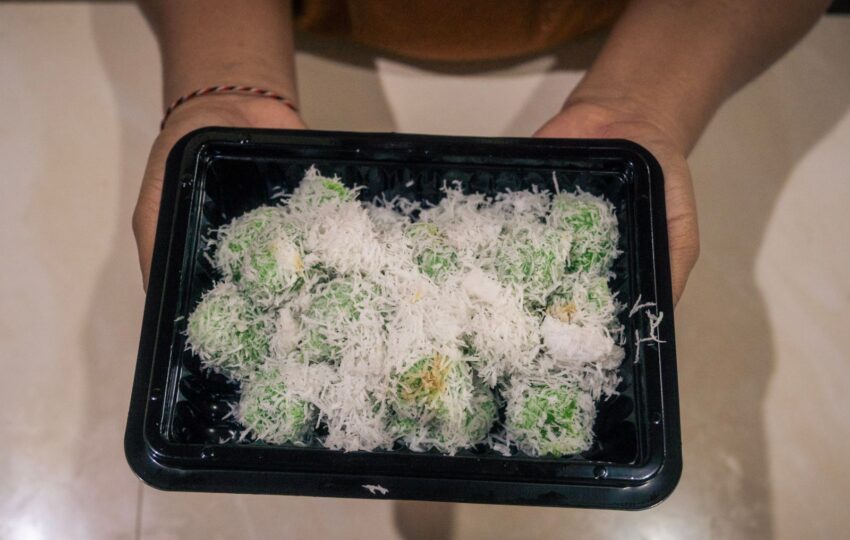 woman holding a box of klepon balinese rice flour and coconut snacks