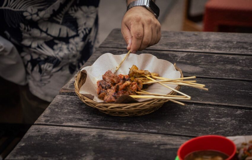 man taking a stick of sate to taste